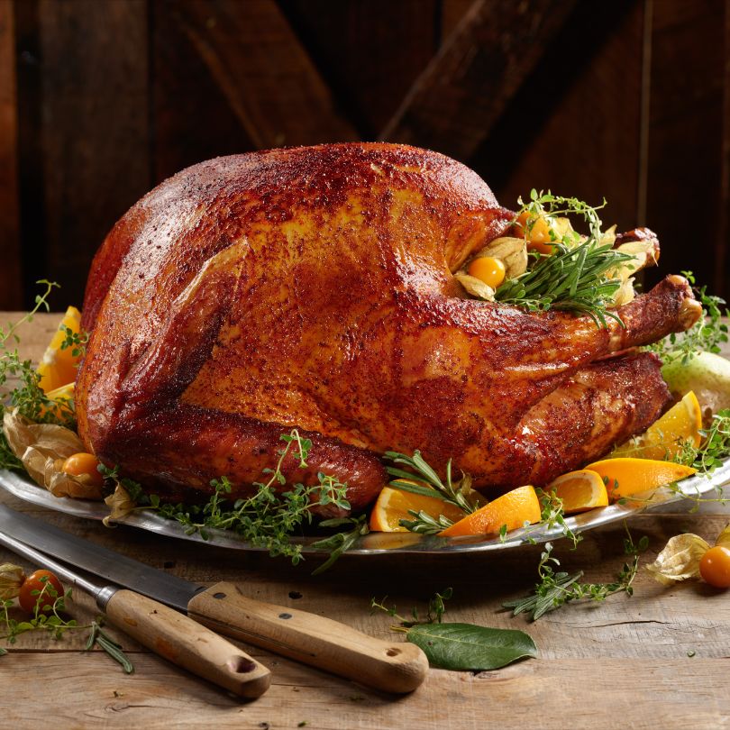 Golden roasted turkey on a silver platter, garnished with rosemary and thyme with orange wedges around it on a rustic table.